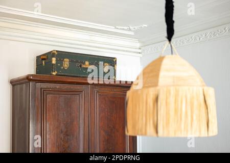 Nahaufnahme eines orientalischen Kronleuchters auf dem Hintergrund eines burgunderfarbenen antiken Kleiderschranks aus Holz und eines grünen Koffers in einem gemütlichen Zimmer mit Stuckhaftung Stockfoto