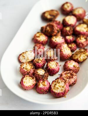 Im Ofen gebackene rosa Radieschen auf einer ovalen Platte. Weißer Hintergrund Stockfoto