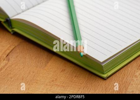 Ein liniertes Notizbuch mit grünem Bleistift. Bereit, Notizen zu machen, Ideen zu skizzieren und Pläne zu schreiben. Stift und Papier bereit. Stockfoto