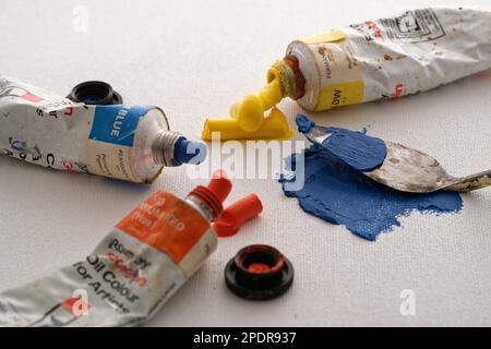 Farbige Ölfarben und ein Palettenmesser auf einem Hintergrund aus Leinwand. Blau, Rot und Gelb, um ein Bild zu machen. Der kreative Prozess. Stockfoto