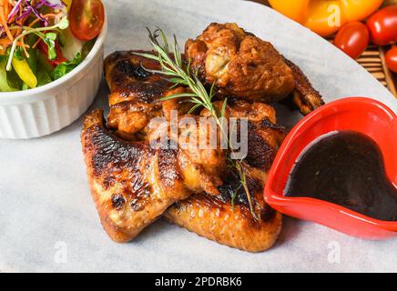 Gebratene Hähnchenflügel serviert Gemüsesauce und Sauce auf weißem Teller, Nahaufnahme von der Seite Stockfoto