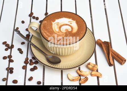 Eine Tasse Nuss-Cappuccino mit Löffel und Zucker auf einem weißen Holztisch mit seitlichem Blick Stockfoto