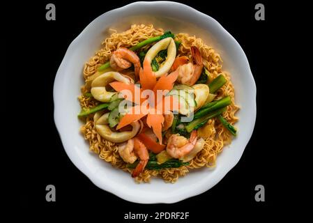 Garnelen und Tintenfisch mit Nudeln und Gemüse in einer weißen Schüssel, isoliert auf schwarzem Hintergrund, Draufsicht Stockfoto