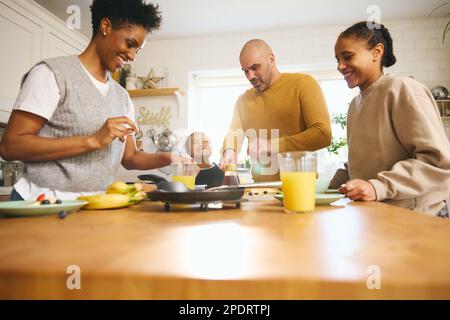 Familie und Junge mit Down-Syndrom, die Pfannkuchen zum Frühstück machen Stockfoto