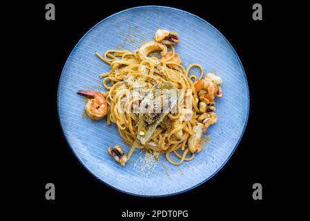 Pasta Carbonara mit Meeresfrüchten auf blauem Teller mit Garnelen isoliert auf schwarzem Hintergrund, Draufsicht Stockfoto