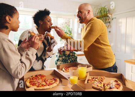Familie isst Pizza zum Mitnehmen zu Hause, Mann füttert Frau Stockfoto