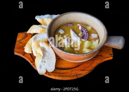 Gedünsteter Tintenfisch mit Kartoffeln in einem Topf, isolierter schwarzer Hintergrund, Seitenansicht Stockfoto