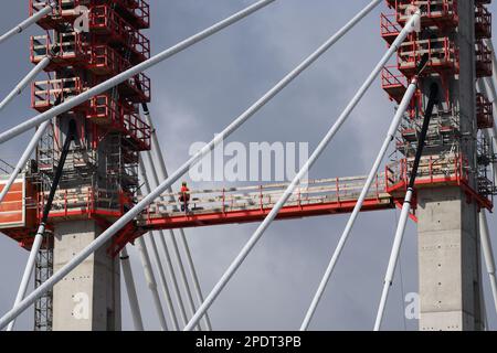15. März 2023, Sachsen-Anhalt, Magdeburg: Ein Arbeiter geht über eine Verbindungsbrücke zwischen den Pylonen des Neubaus der Brücke in Magdeburg. Aufgrund des hohen Wasserspiegels der Alten Elbe musste der Bau der neuen Elbbrücke angepasst werden. Zuvor wurden im Flussbett angeordnete HD-Kräne zum Anheben der Brückenkomponenten verwendet. Seit Anfang Februar ist der Wasserstand auf der Baustelle so hoch, dass eine Baustraße überflutet wurde. Nun soll ein großer Kran am östlichen Dämpfer errichtet werden, um die Brückenabschnitte von dort anzuheben. Foto: Klaus-Die Stockfoto