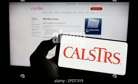 Person, die ein Mobiltelefon mit dem Logo des California State Teachers Retirement System (CalSTRS) auf dem Bildschirm vor der Webseite hält. Konzentrieren Sie sich auf das Display des Telefons. Stockfoto