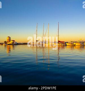Sonnenaufgang an der Almerimar Marina mit dem goldenen Licht der aufgehenden Sonne, das von den Booten im ruhigen Wasser schwebt, während der Leuchtturm gu steht Stockfoto