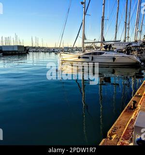 Am frühen Morgen in der Almerimar Marina in Spanien mit der niedrigen Sonne auf dem Rumpf einer Yacht und den Booten, die sich im ruhigen blauen Wasser unter einem Cl Stockfoto