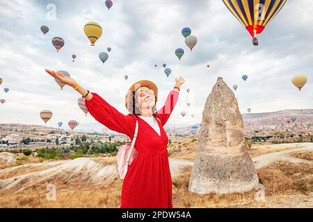 Ein Mädchen in einem Kleid, das sich in den atemberaubenden Anblick fliegender Heißluftballons in Kappadokien, dem Paradies für Reisende, eingefangen hat. Stockfoto