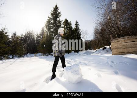 Der Junge schuf Schneekugel für Schneemann. Spielen Sie im Winter im Freien mit Schnee in den Bergen. Stockfoto