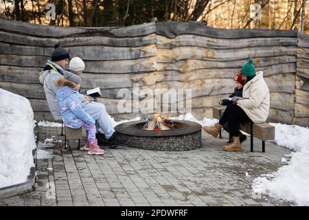 Eine Familie mit drei Kindern, die am Lagerfeuer saß und im Wald Bücher über den Winter las. Kinder auf dem Land. Stockfoto