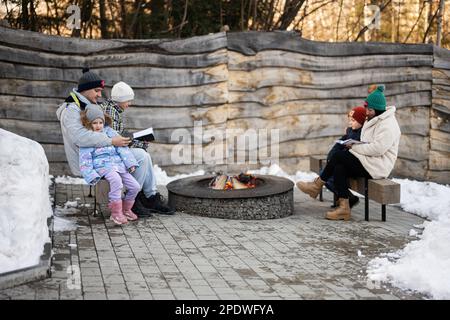 Eine Familie mit drei Kindern, die am Lagerfeuer saß und im Wald Bücher über den Winter las. Kinder auf dem Land. Stockfoto