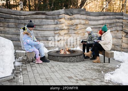 Eine Familie mit drei Kindern, die am Lagerfeuer saß und im Wald Bücher über den Winter las. Kinder auf dem Land. Stockfoto