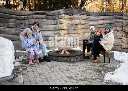 Familie mit drei Kindern, die im Winter am Lagerfeuer im Wald saßen. Kinder auf dem Land. Stockfoto