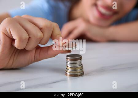 Junge Frau stapelt Münzen am Tisch, konzentriert euch auf die Hand. Kostenersparnis Stockfoto