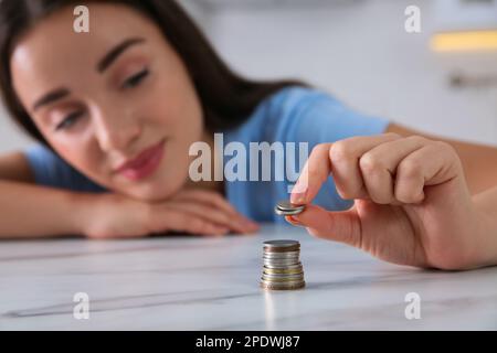 Junge Frau stapelt Münzen am Tisch, konzentriert euch auf die Hand. Kostenersparnis Stockfoto