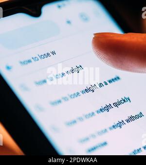 Nahaufnahme der Rückseite einer Frau, die auf einem Smartphone nach Gewichtsverlust sucht Stockfoto