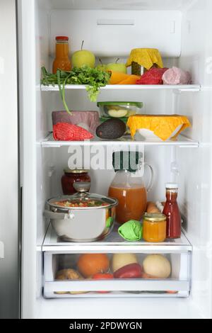 Offener Kühlschrank mit vielen verschiedenen Produkten, verpackt in Bienenwachs-Lebensmittelverpackungen Stockfoto