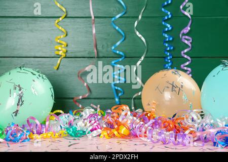 Farbenfrohe Luftschlangen, Ballons und Konfetti auf pinkfarbenen Holztisch Stockfoto