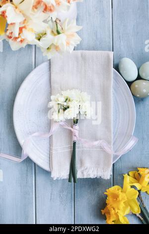 Ein Urlaubsort mit Teller, Eiern, Serviette und Narzissen auf einem blauen Ostertisch. Aufnahme von flach liegender oder oberer Position. Blumen Stockfoto