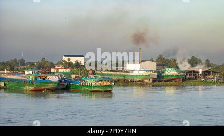 Motorisierte Lastkähne an der Seite des Mekong-Flusses neben Fabriken und Verschmutzung in der Nähe von Long Xuyen im Mekong-Delta, Vietnam. Stockfoto