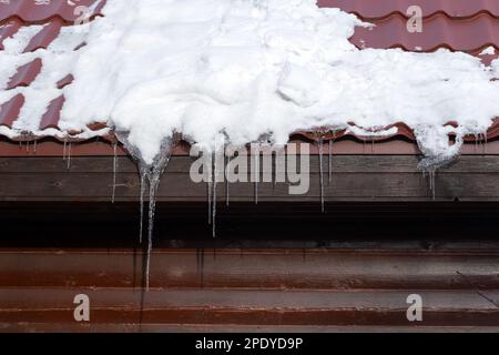 Eiszapfen hängen an einem sonnigen Tag auf dem weißen Dach eines Landhauses Stockfoto