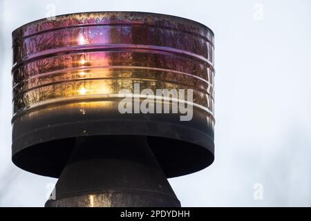 Runder, glänzender Metallkamin mit Hitzetönung und Ruß unter blauem Himmel bei einem Tagesfoto Stockfoto