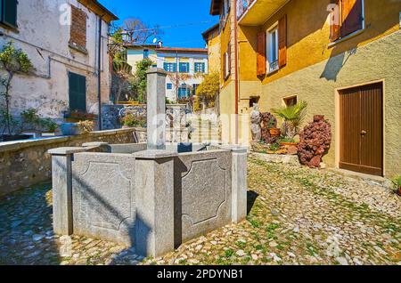 Alte Häuser, Pflanzen in Töpfen und kleiner Brunnen inmitten des mittelalterlichen Piazza Rusciett in Castello, Valsolda, Lombardei, Italien Stockfoto