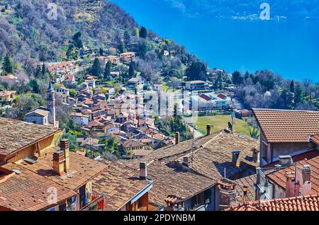 Die kleine Loggio-Siedlung mit Glockenturm der Kirche San Bartolomeo und kleinen Häusern hinter den Dächern und Schornsteinen von Castello, Valsolda, Italien Stockfoto