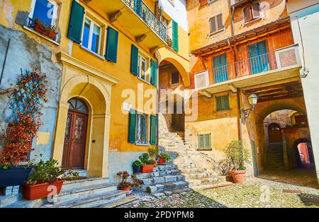 Die alte Architektur von Oria mit bunten Hauswänden, grünen Pflanzen in Töpfen und Steintreppen, die zu den verschiedenen hügeligen Straßen, Valsolda, Italien, führen Stockfoto