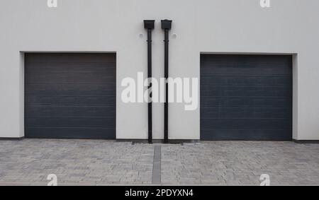 Zwei graue Rollläden in der Garage an der weißen Fassade. Abstand auf Gehwegen, Auffahrt. Stockfoto