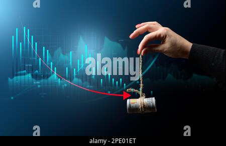 Eine weibliche Hand, die mit einem Seil und einem Diagramm mit rückläufigen Indikatoren Dollar hält, das Konzept der Finanzkrise, den sich verschlechternden Lebensstandard, f Stockfoto