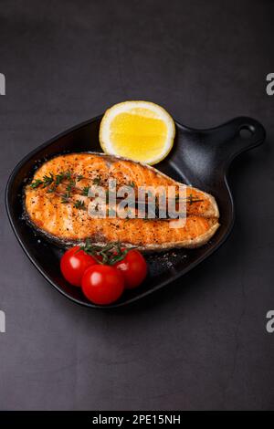 Gegrillter Lachs mit Kirschtomaten, Thymian und Zitrone auf einer kleinen schwarzen Grillpfanne. Gebratener Fisch ist ein traditionelles Gericht der Hausmannskost und Restaurants. Stockfoto