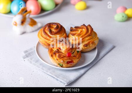 Craffin Mini (Craffin) mit Rosinen und kandierten Früchten. Traditioneller Osterkuchen. Im Hintergrund sind bemalte Eier und ein Osterhasen. Stockfoto