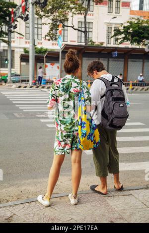 Ho Chi Minh City, Vietnam - 18. August 2019: Ein junges Touristenpaar auf einem Fußgängerweg von hinten. Ein Mann und eine Frau in lässiger Sommerkleidung trav Stockfoto