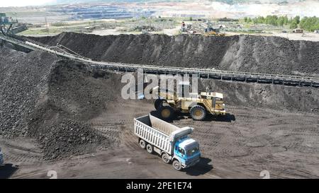 Radlader, der Kohle auf Lkw lädt und auf einer riesigen Bergbaustelle arbeitet. Stockfoto