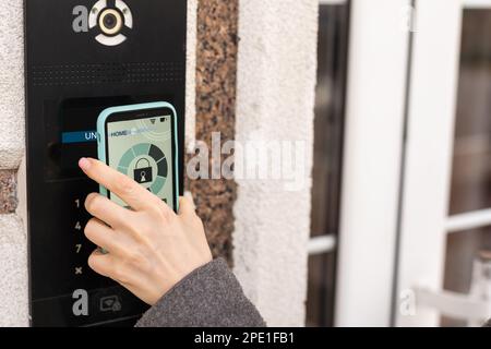 Frau, die smartlock an der Eingangstür mit einem Smartphone verriegelt. Konzept der Verwendung intelligenter elektronischer Schlösser mit schlüssellosem Zugang. Stockfoto