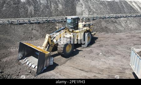 Radlader, der Kohle auf Lkw lädt und auf einer riesigen Bergbaustelle arbeitet. Stockfoto