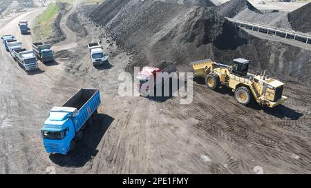 Radlader, der Kohle auf Lkw lädt und auf einer riesigen Bergbaustelle arbeitet. Stockfoto