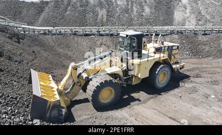 Radlader, der Kohle auf Lkw lädt und auf einer riesigen Bergbaustelle arbeitet. Stockfoto