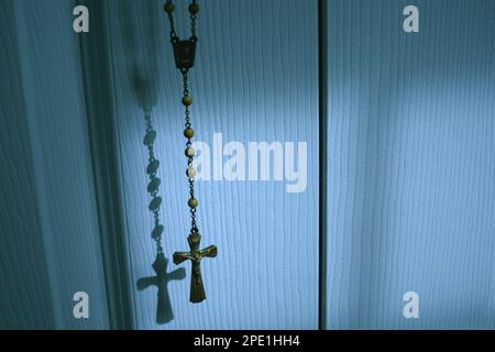 Katholische Kruzifixanhänger und Schranktür im sanften Mondlicht Stockfoto