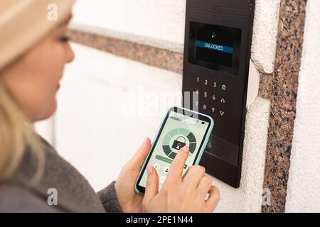 Frau, die smartlock an der Eingangstür mit einem Smartphone verriegelt. Konzept der Verwendung intelligenter elektronischer Schlösser mit schlüssellosem Zugang. Stockfoto