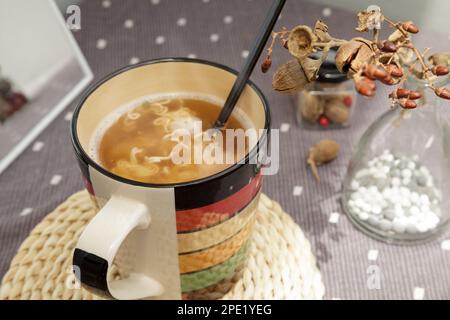 Einfach heiße Instantnudeln in einer Tasse mit einer Gabel gekocht, fertig zum Essen. Günstiges, schnelles Frühstück zu Hause allein in einer gemütlichen Atmosphäre Stockfoto