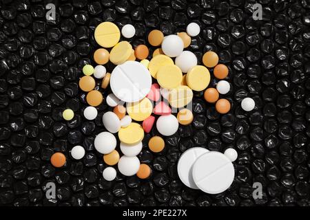 Ein bunter Stapel verschiedener Pillen auf Schwarz. Verschreibungspflichtige Medikamente gegen Kopfschmerzen, Schmerzen, Krankheit. Viele verschiedene weiße, gelbe, rote Tabletten Stockfoto