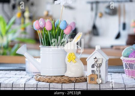 Schlüssel zum Haus eines gemütlichen Hauses mit Osterdekor mit Hase und Eiern auf dem Tisch der Küche. Gebäude, Entwurf, Projekt, Umzug in ein neues Haus, Hypothek, Versicherung Stockfoto