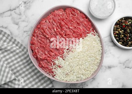 Schüssel mit Forcemeat mit Reis und Gewürzen zur Zubereitung von gefüllten Kohlrollen auf einem weißen Marmortisch, flach liegend Stockfoto