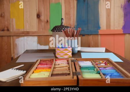 Leere Papierbögen, bunte Kreidepastelltöne und Malstifte auf Holztischen im Innenbereich. Der Arbeitsplatz moderner Künstler Stockfoto